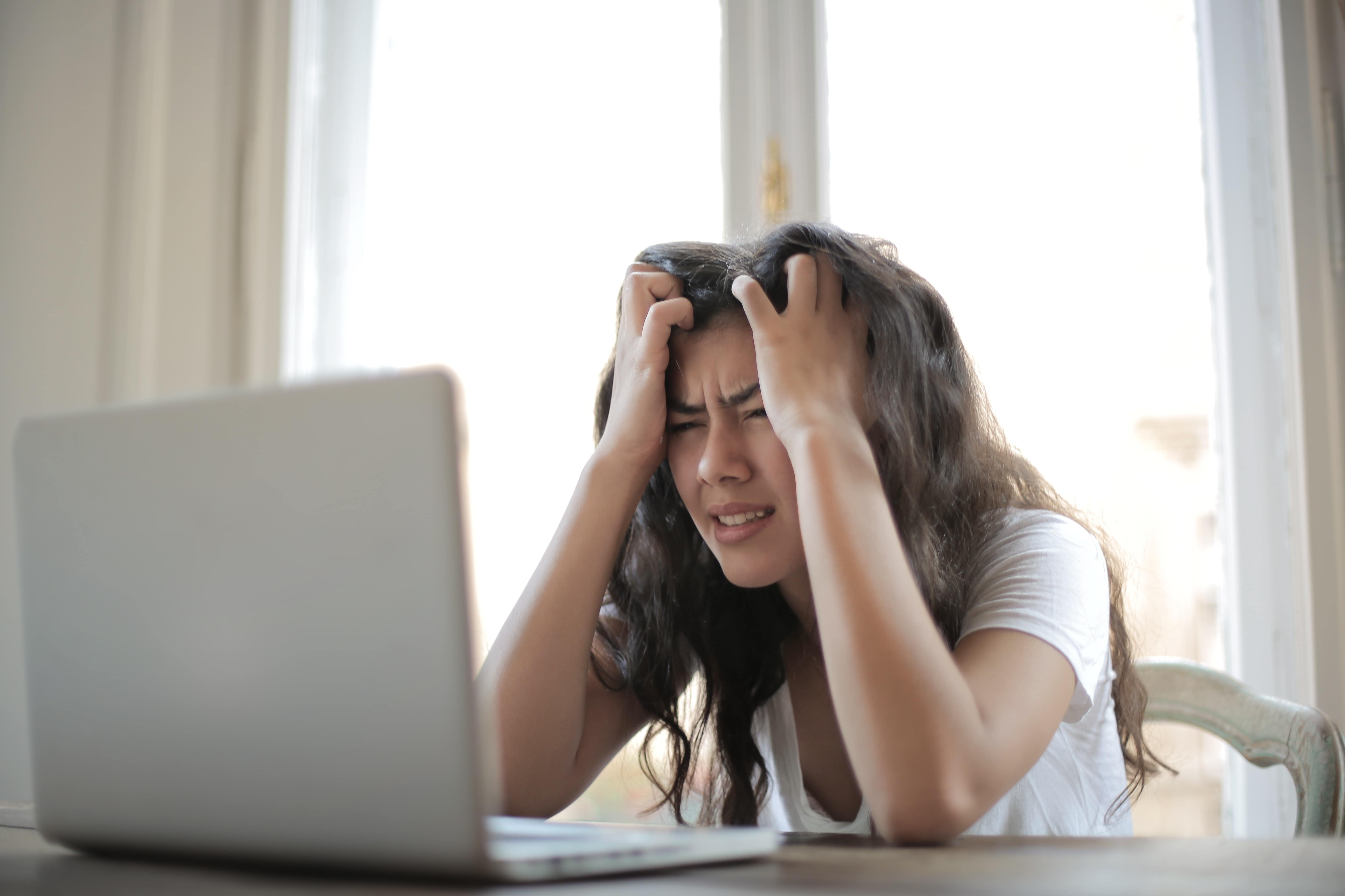 Woman in white shirt pulling hair out in frustration with her laptop
