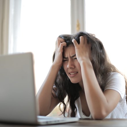 Woman in white shirt pulling hair out in frustration with her laptop