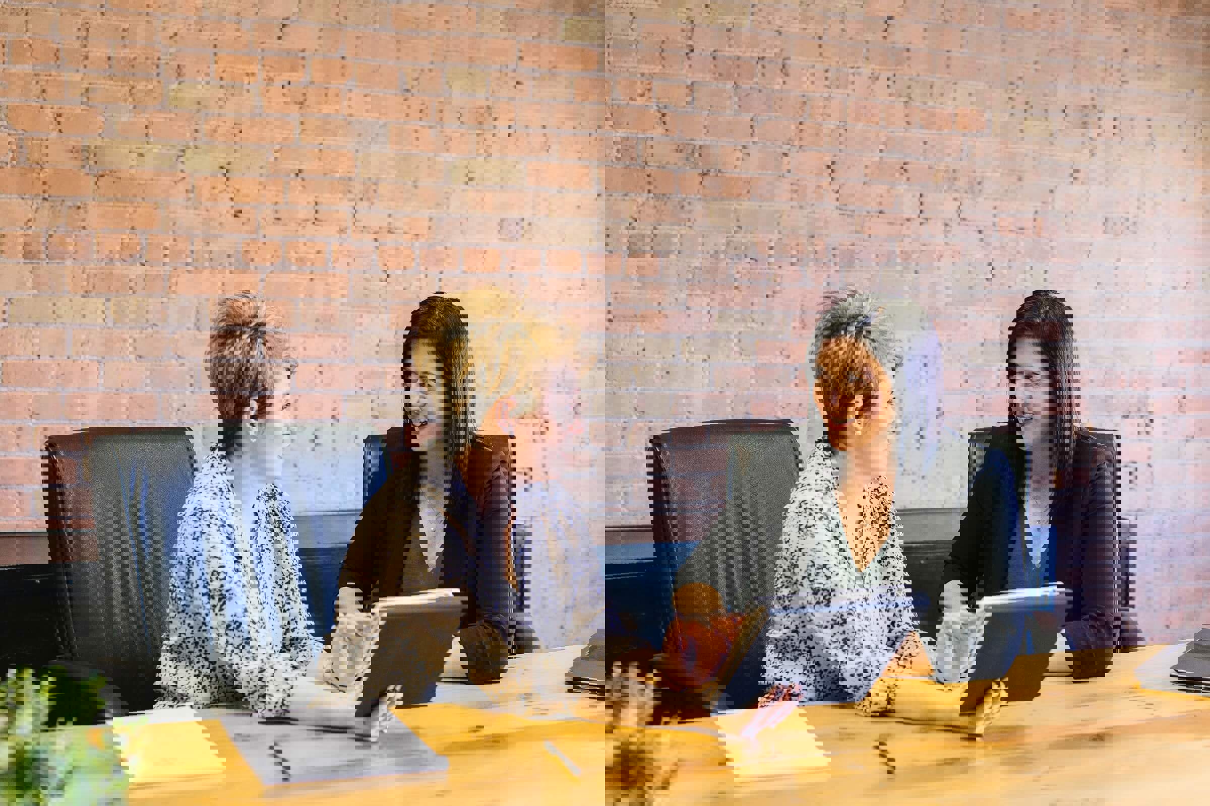 Two female colleagues discussing something at a boardroom table with a tablet
