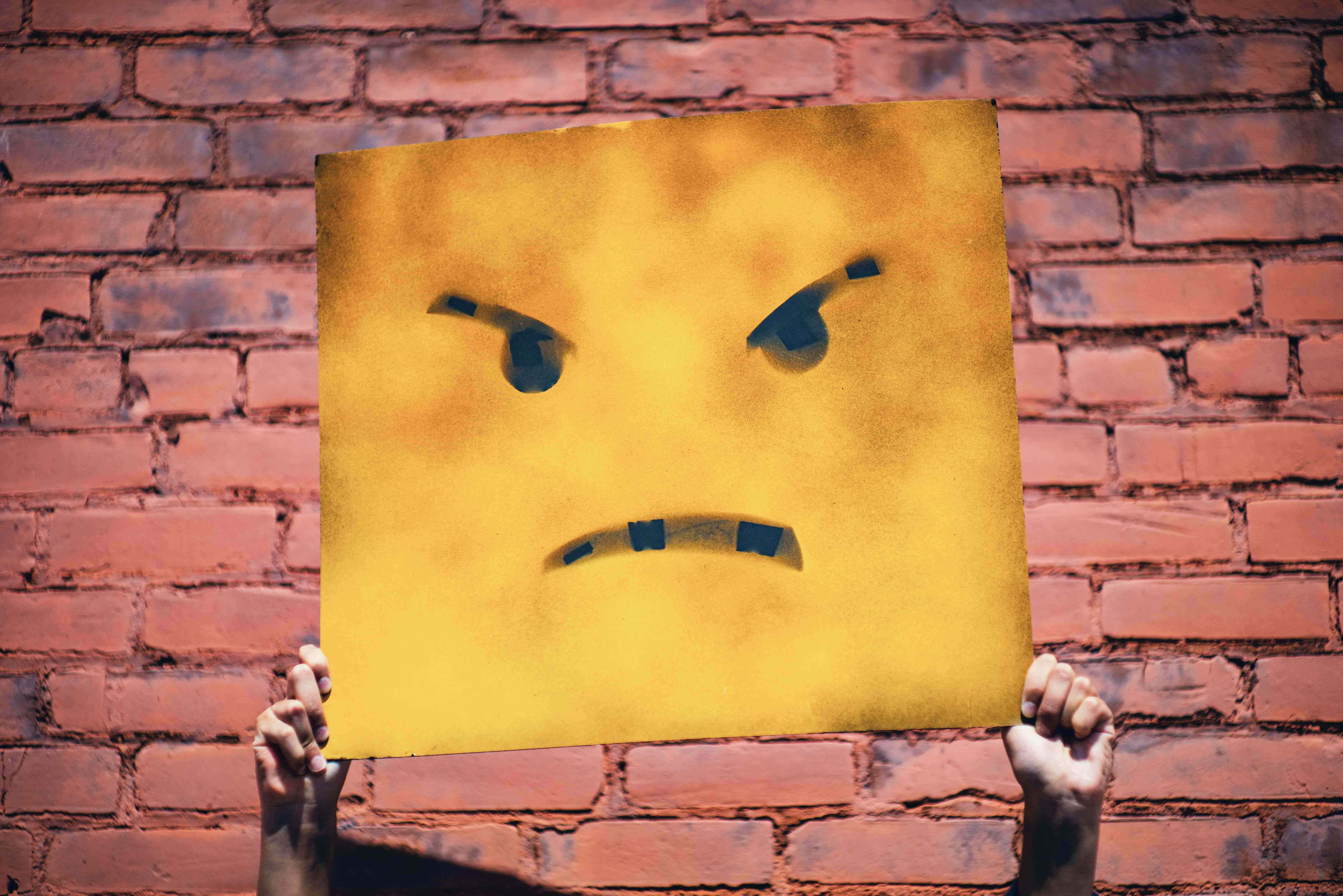 Someone holding a cardboard with a drawing of an angry face
