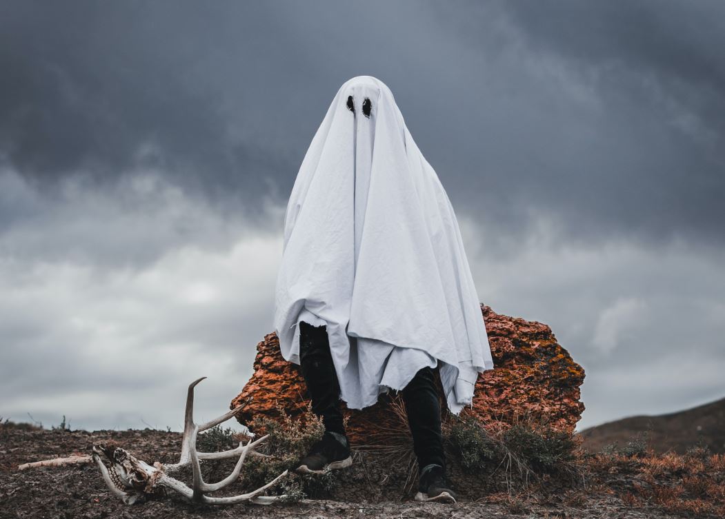 Man with sheet over his head sitting in a gloomy setting