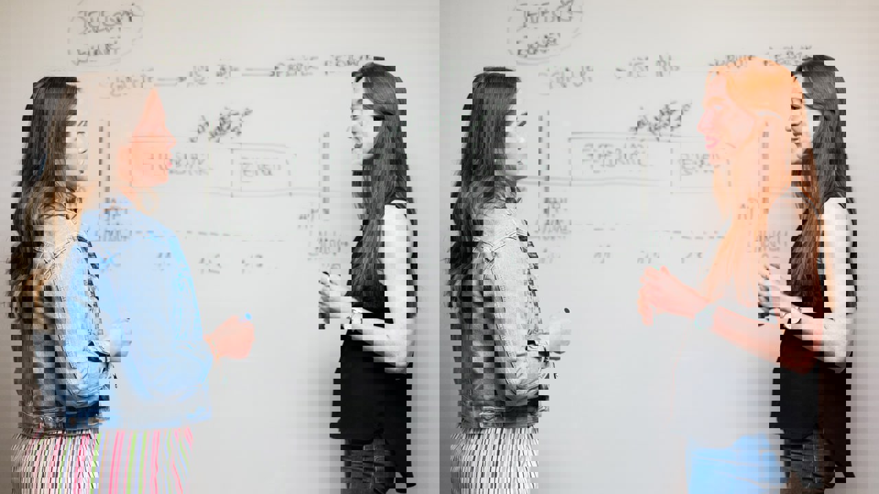 two woman writing on a whiteboard